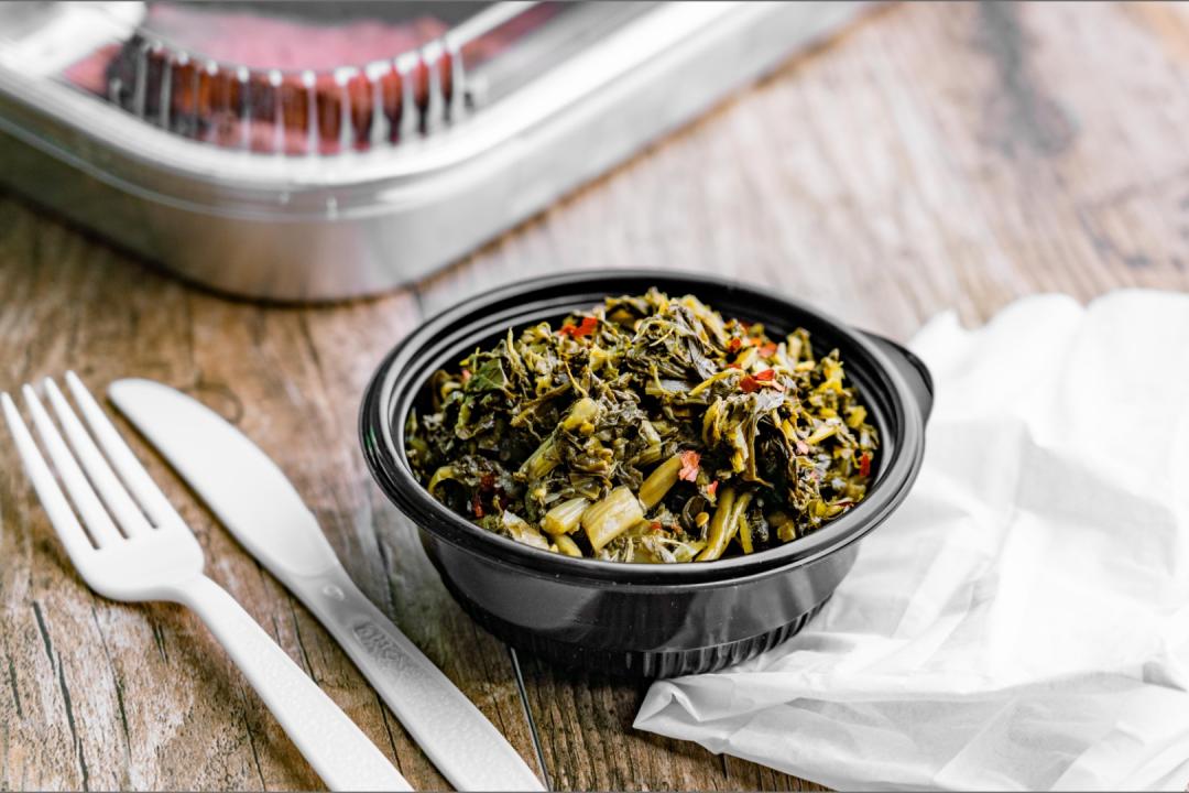 Southern Style Greens in a takeout-style container with plastic cutlery and napkin
