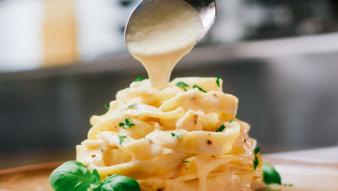 A spoon dripping vegan alfredo sauce onto a pasta dish