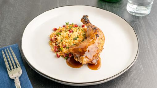 A plate with bourbon roasted chicken leg and cous cous